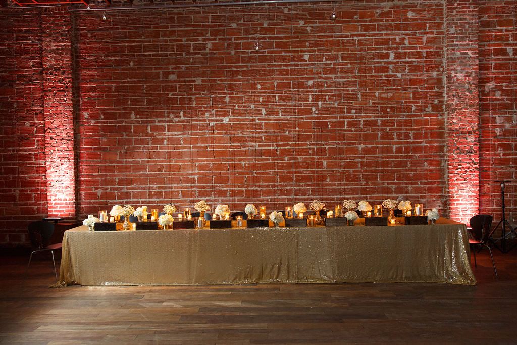Long Feasting Table with Gold Sparkle/Sequin Linens with Candlelight and Elegant White Hydrangea and Babysbreath Centerpieces | Wedding Reception Decor | Exposed Brick Walls at St. Pete Wedding Venue NOVA 535